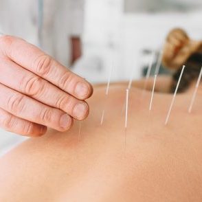Acupuncturist inserting a needle into a female back. patient having traditional Chinese treatment using needles to restore an energy flow through specific points on the skin.
