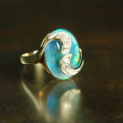 Woman's opal triplet and diamond ring on a dark reflective background.